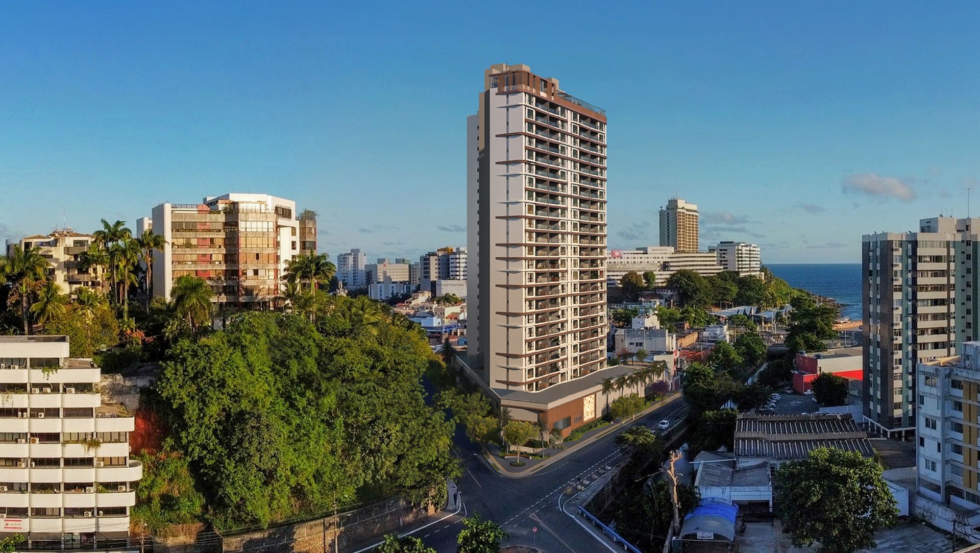 Vista aérea do Rivê Rio Vermelho, um arranha-céu residencial proeminente entre outros edifícios, com vista para o oceano e rodeado por vegetação.