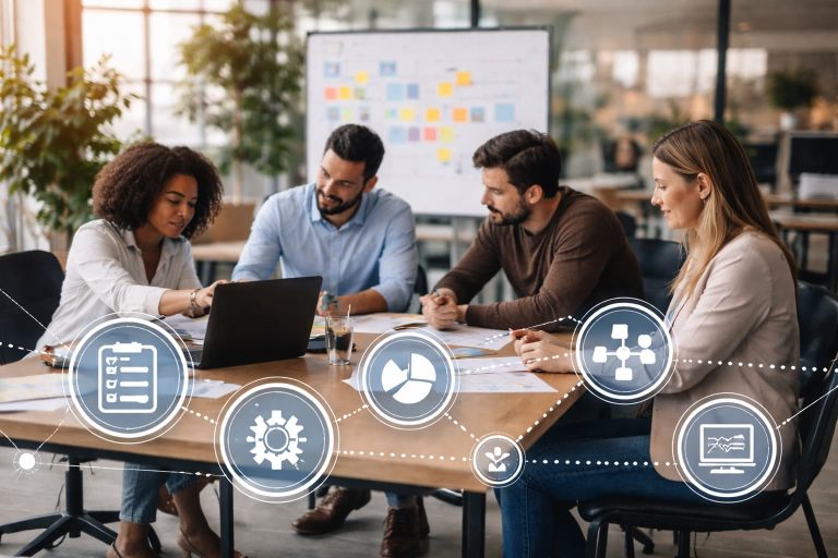 Grupo de profissionais reunido em mesa de trabalho analisa informações em laptop e documentos, com painel visual ao fundo em ambiente corporativo